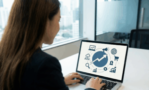 Femme d'affaires vue de dos analysant sur l'écran de son ordinateur portable un schéma graphique illustrant une stratégie de pénétration digitale et de croissance.